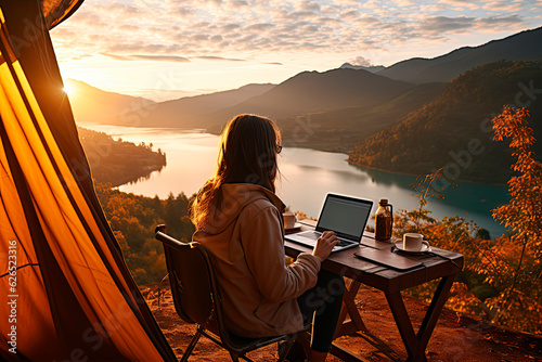 Young woman freelancer traveler working online using laptop and enjoying the beautiful nature landscape with mountain view at sunrise #626523316