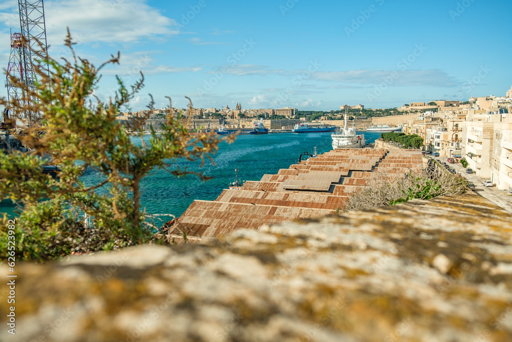 Roofs of warehouses in foreground, cargo ship in front of historic old town of Valletta