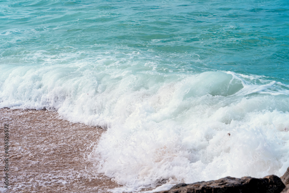 Fototapeta premium a wave with foam rolling onto the beach shore