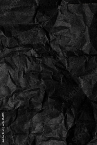 A sheet of black wrinkled paper. Texture of black crumpled paper. Dark paper background with chaotic bends.