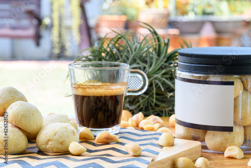 Macadamia nut and cookies in plastic box next to black coffee on wooden table in backyard