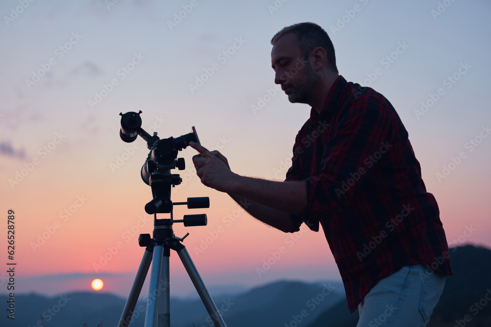 Astronomer looking at the sun with a telescope and using a cellphone.