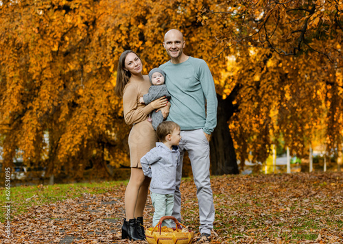 A family with a son and daughter against the background of a large yellow tree. Beautiful Golden Autumn