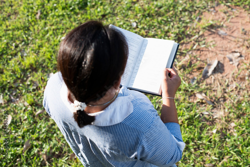 Girl reading a book in the front yard Female student portrait, education concept Happy cute kid smiling with learning.