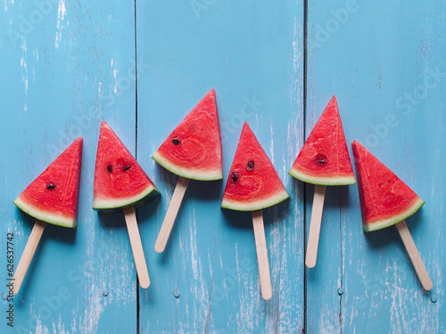 Slice watermelon popsicle sticks top view on blue color wooden table for summer fruit concept.