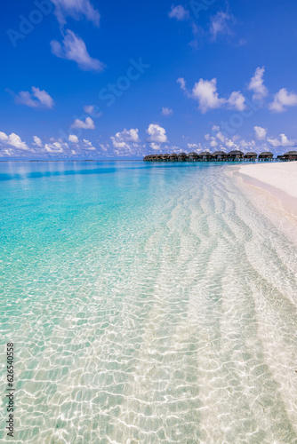 Maldives island, luxury water villas resort. Beautiful blue sunshine sky closeup ocean waves lagoon beach background. Summer vacation wallpaper and travel concept. Paradise panoramic coast landscape