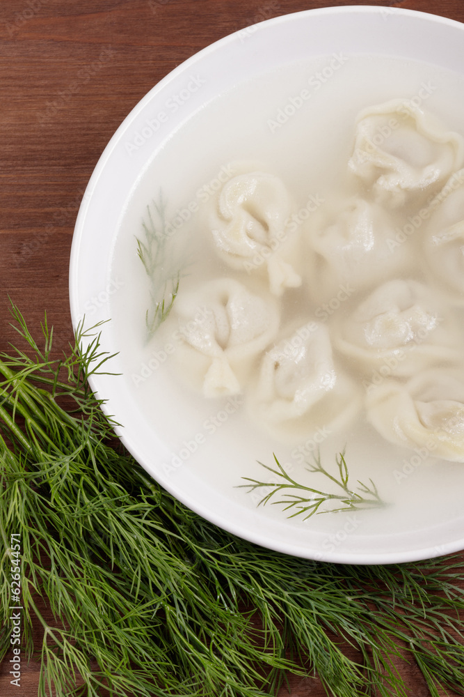 Bouillon with homemade pelmeni and fresh dill. Soup with dumplings and herbs. Top view.