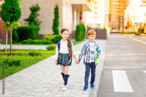 a boy and a girl with briefcases or backpacks walk from school by the hand and smile, go back to school, brother and sister study in the same class