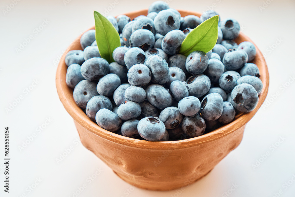 A full jug of fresh large blueberries with leaves on a white background. Berries, healthy food. Selective focus. Side view. A full jug of fresh large blueberries with leaves on a white background. Berries, healthy food. Selective focus. Side view.