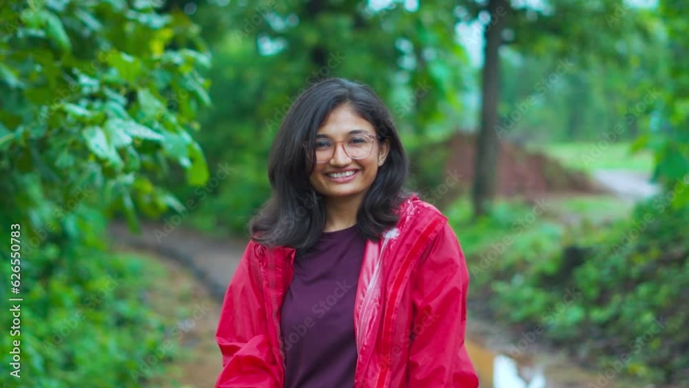 Portrait of smiling Indian girl looking at camera while standing against lush green trees at Saputara, Gujarat, India. Teenager girl wearing raincoat in monsoon. Travel in rainy weather. Portrait of smiling Indian girl looking at camera while standing against lush green trees at Saputara, Gujarat, India. Teenager girl wearing raincoat in monsoon. Travel in rainy weather.