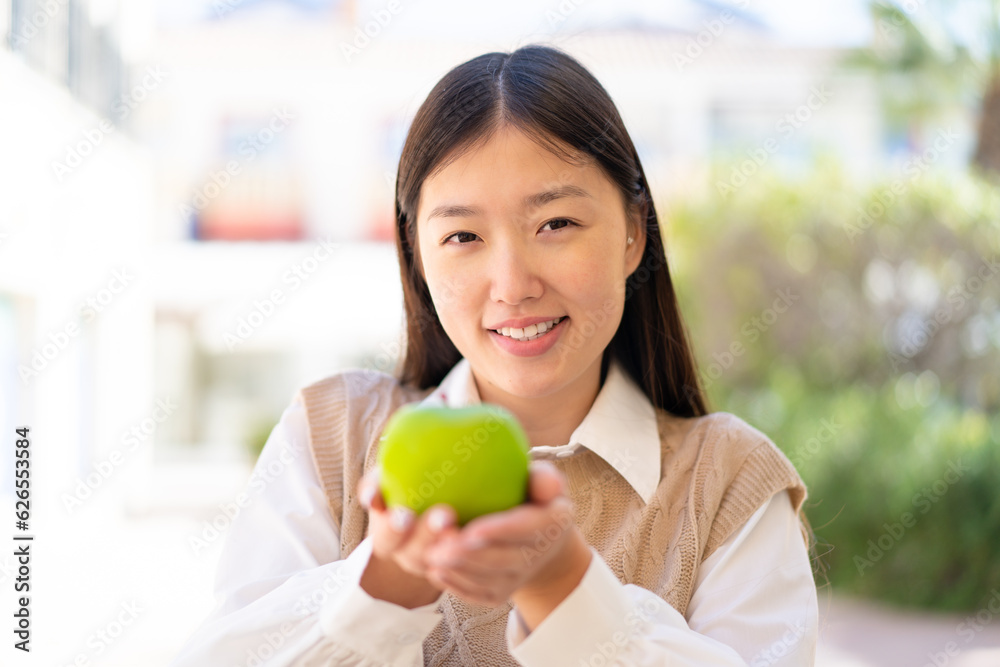 Pretty Chinese woman at outdoors holding an apple with happy expression Pretty Chinese woman at outdoors holding an apple with happy expression