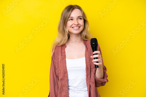 Fotografie Young singer caucasian woman picking up a microphone isolated on yellow backgrou