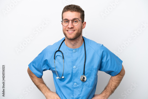 Young surgeon doctor caucasian man isolated on white background posing with arms at hip and smiling