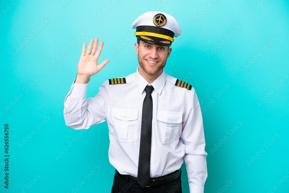 Airplane caucasian pilot isolated on blue background saluting with hand with happy expression Airplane caucasian pilot isolated on blue background saluting with hand with happy expression