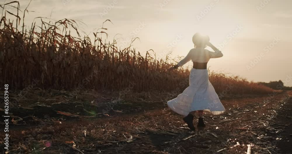 A female farmer in a dress walks among the fields of corn