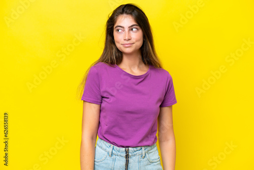 Young caucasian woman isolated on yellow background making doubts gesture looking side