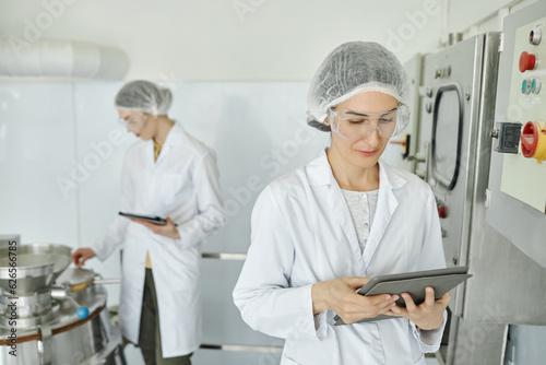 Portrait of two women wearing lab coats working at factory in food or pharma production, copy space