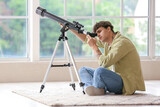 Young man with telescope sitting on floor