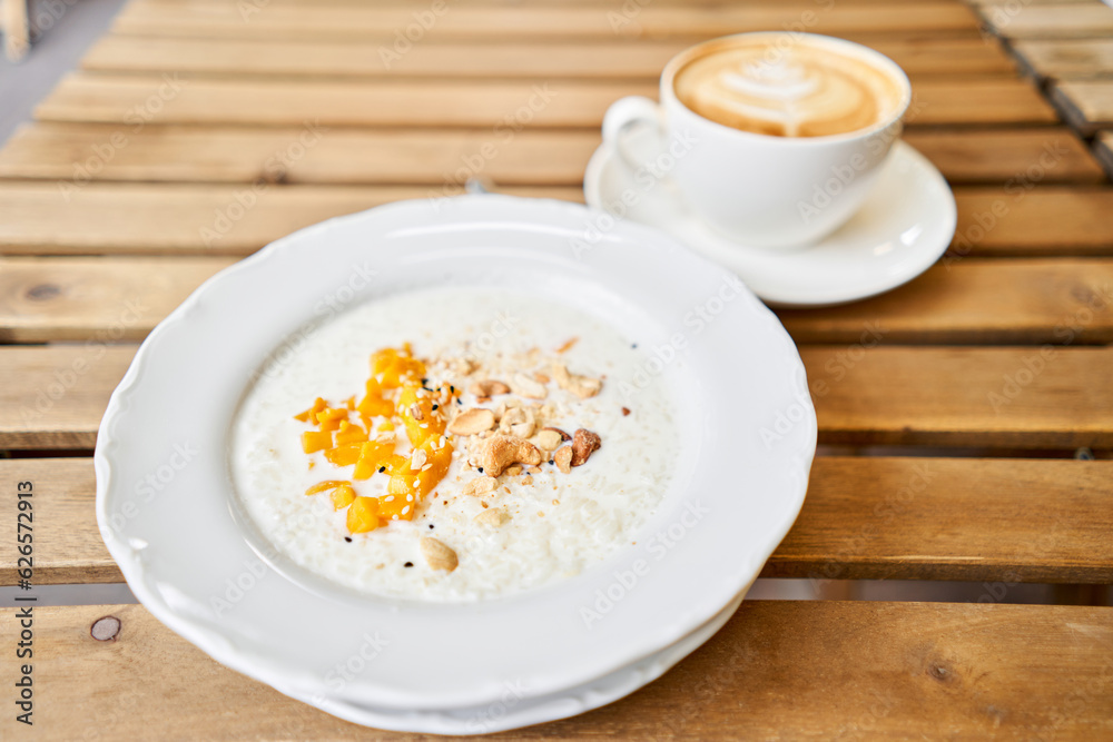 Breakfast in cafe on a sunny morning, on the summer veranda. Cappuccino coffee and rice porridge with mango, Cashews, sesame seeds. enjoying breakfast. Breakfast in cafe on a sunny morning, on the summer veranda. Cappuccino coffee and rice porridge with mango, Cashews, sesame seeds. enjoying breakfast.