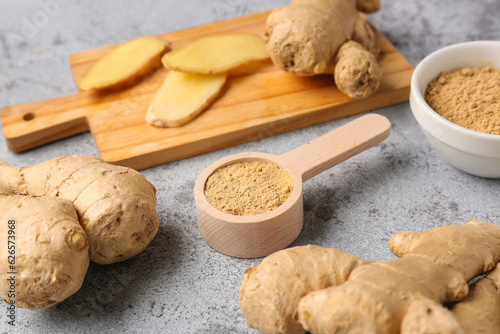 Fresh ginger roots, bowl and wooden spoon with dried powder on blue background