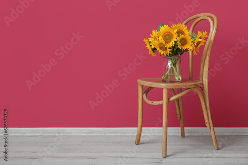 Vase with beautiful sunflowers on chair near burgundy wall in room