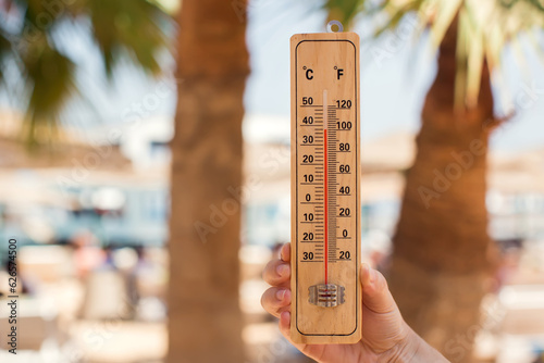 Thermometer in hand on a beach background showing high temperature. Hot weather and climate concept