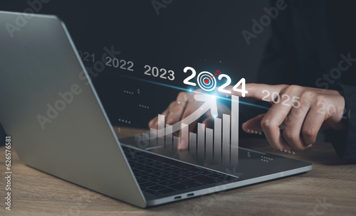 Target and goal of 2024 year business new year concept. Businessman touching future showing glowing virtual technical investment graph chart for analysis stock market of 2024.