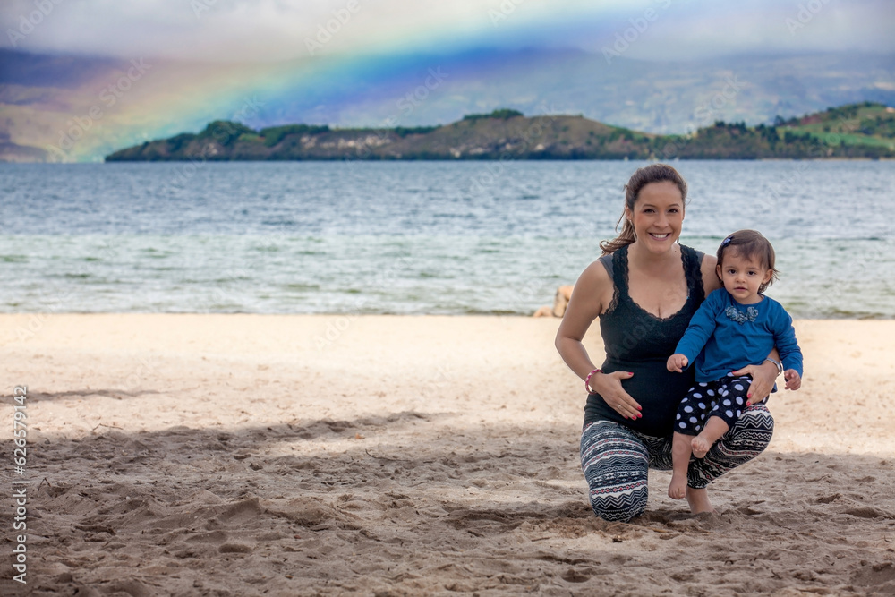 Young pregnant woman having fun with her baby girl at the beautiful white beach of Lake Tota located in the department of Boyaca at 3,015 meters above sea level in Colombia
