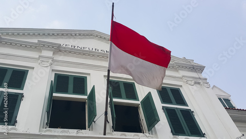 The Indonesian red and white flag flutters on top of the old Dutch heritage building photo