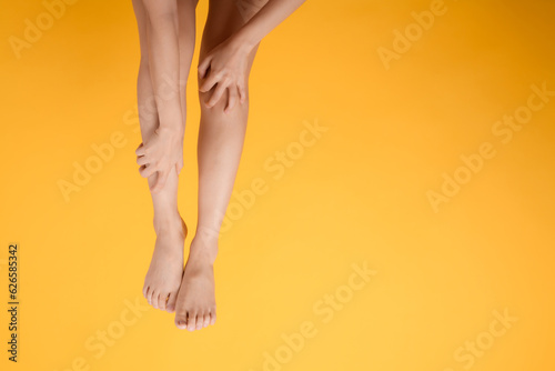 Explore legs healthcare with a close up of woman's legs, hands holding her pained legs on a vibrant yellow background. Concept of leg pain relief. © Jirawatfoto