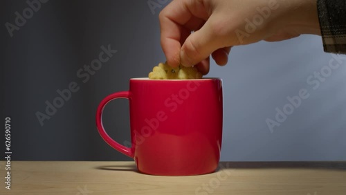 A man's hand dunks a biscuit - cookie - into a hot beverage in a bright red coffee mug.