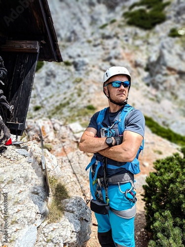 Man dressed in climbing gear. He wears a white helmet and sunglasses. He carries a harness and ferratas lanyards for climbing photo