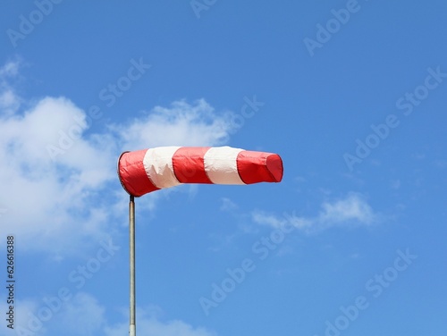 Windsock indicator of wind. Horizontally flying windsock ( wind vane ) with blue sky and white clouds in the background. Wind cone indicating wind and force.