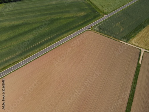 View from above of agriculture land with green growing crop fields, brown plowed arable fields and a asphalt road in the middle
