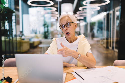 Crazy senior woman sitting with laptop in meeting room in modern office