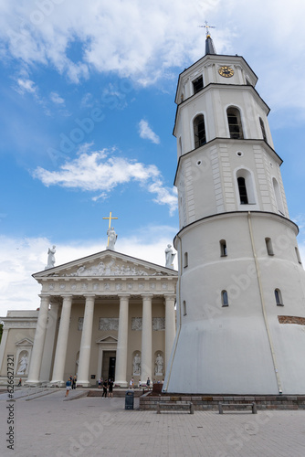 Vilnius Cathedral, with people walking through the square, on a day with a blue sky and some clouds.