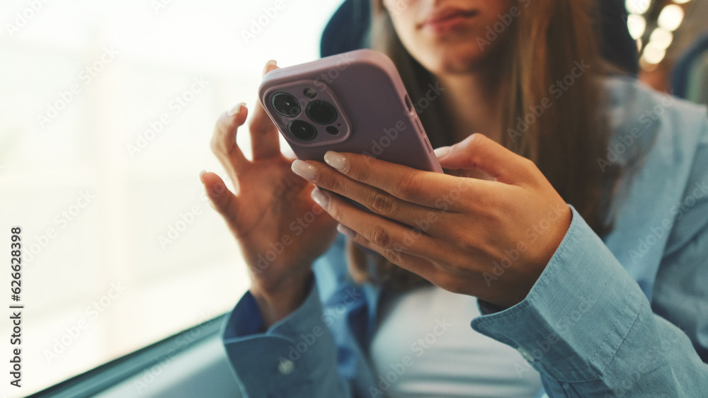 Close-up of hands cute girl with long brown hair, dressed in blue shirt, scrolls on smartphone screen during her train ride