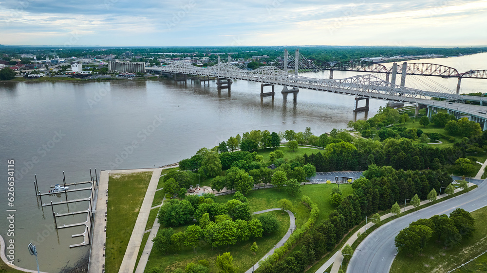 White truss, suspension bridges with rusty arch bridge on Ohio River near docks and greenery aerial White truss, suspension bridges with rusty arch bridge on Ohio River near docks and greenery aerial