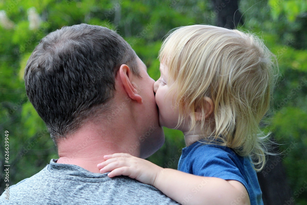 The daughter kisses her father on the cheek. Father`s face is not visible, he is standing with his back to us. Light photo in nature. The daughter kisses her father on the cheek. Father`s face is not visible, he is standing with his back to us. Light photo in nature.