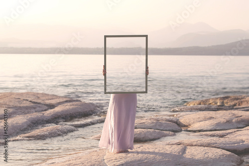Fotobehang woman holding a frame that surreally reflects the landscape , abstract concept
