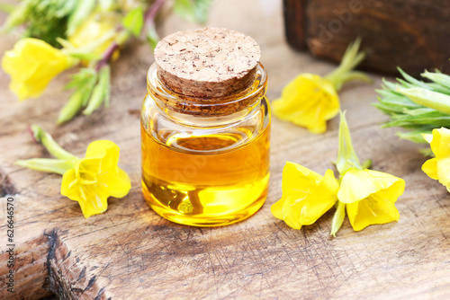 Evening primrose oil in glass bottle with flowers on wooden rustic background, closeup, natural medicine for menopause treatment, for skin care and anti-aging, cosmetic supplement and emollient