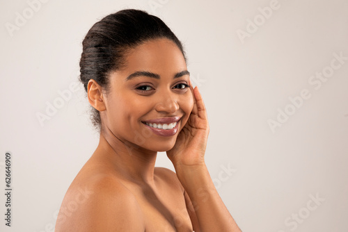Cheerful pretty young half-naked black woman touching face and smiling