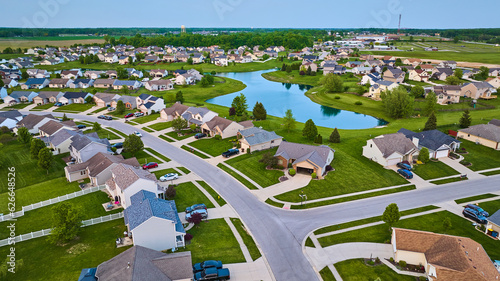 Large pond surrounded by suburban neighborhood HOA houses white picket fence aerial