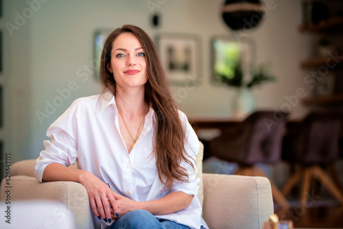 Attractive brunette haired woman wearing white shirt and blue jeans and relaxing in an armchair at home © sepy