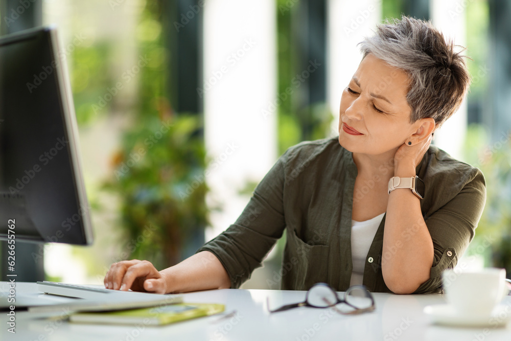 Caucasian mature businesswom sitting at workplace, suffering from neck pain Caucasian mature businesswom sitting at workplace, suffering from neck pain