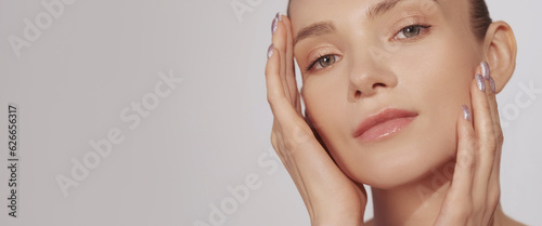 Skin moisturizing. Facial care. Beauty wellness. Woman with nude makeup enjoying touching soft radiant face isolated on beige background empty space.