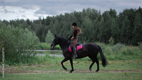 Equestrian sports. A young woman in the saddle, a rider and her horse outdoors, riding in the woods.