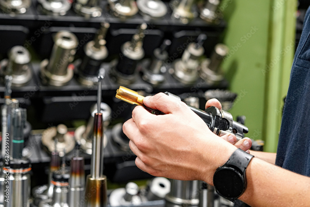 A worker inspects and selects a tap for cutting threads in parts on a CNC milling and turning machine. A worker inspects and selects a tap for cutting threads in parts on a CNC milling and turning machine.