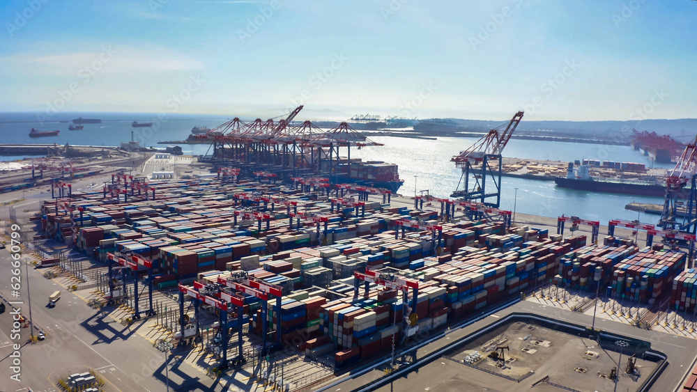 Rows of cargo containers rest atop massive container ships docked at an industrial port. Aerial view cargo ship terminal. Aerial view of shipping container port terminal.