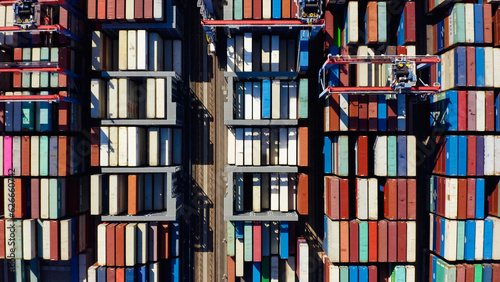 Rows of cargo containers rest atop massive container ships docked at an industrial port. Aerial view cargo ship terminal. Aerial view of shipping container port terminal. 